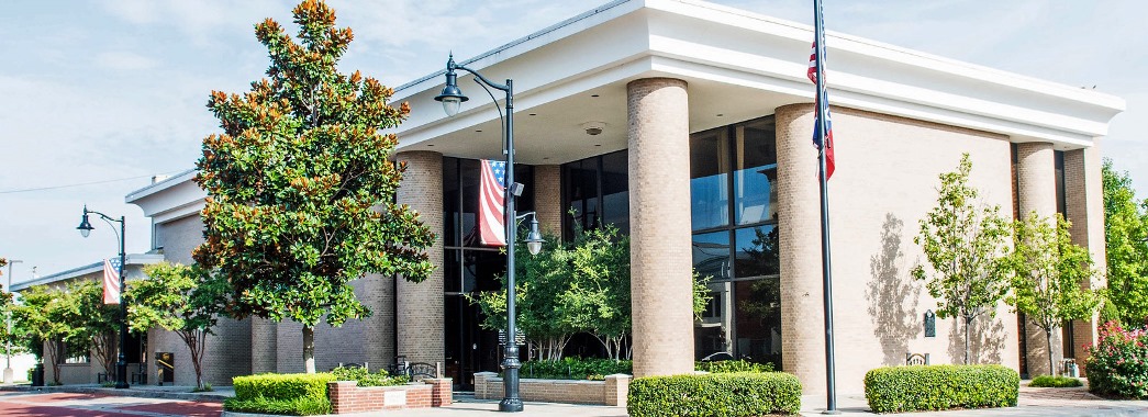 Very large tan brick building with columns and trees in front.